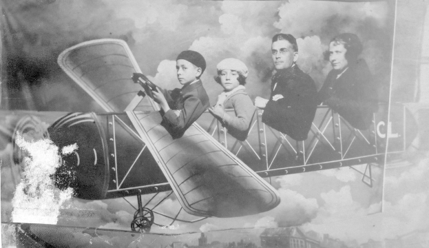 Vier Personen in einem Flugzeug sitzend, eine Person hält eine Waffe in Schwarzweiß.