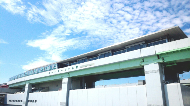 Monorail-Zug fährt über eine Brücke mit Säulen und Geländern, umgeben von Gebäuden und einem bewölkten Himmel.