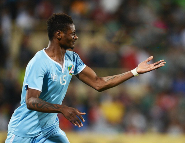 Ein Fußballspieler in einem blauen Trikot feiert nach einem Tor mit ausgestreckten Armen, mit einem unscharfen Hintergrund.