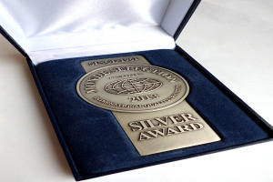 Eine silbern gravierte Auszeichnung in einer blauen Box auf einer weißen Oberfläche.