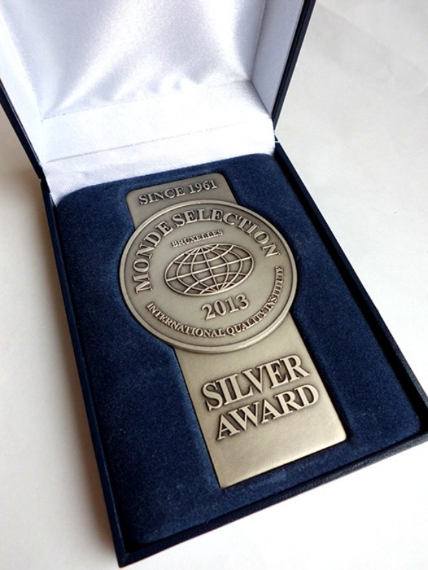 Eine silbern gravierte Auszeichnung in einer blauen Box auf einer weißen Oberfläche.