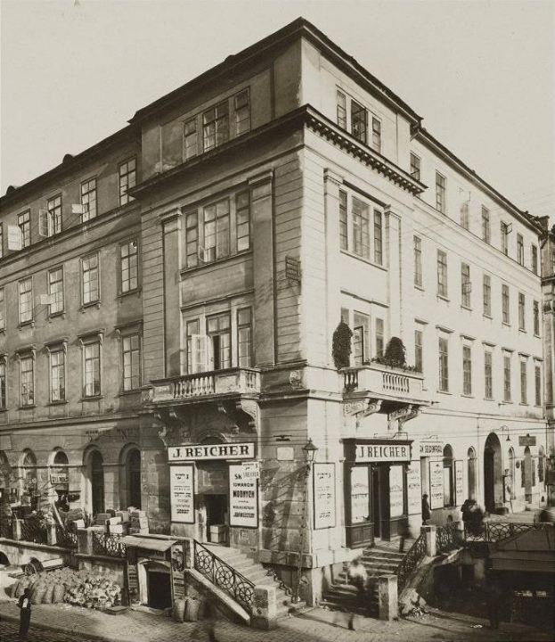 Altes Backsteingebäude mit der Aufschrift 'J Reicher Hotel' in Berlin, das Fenster, Treppen mit Geländern, Schilder, Topfpflanzen, einige Menschen und einen sichtbaren Himmel im Hintergrund zeigt.