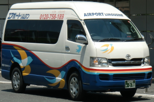 Ein weißer und blauer Van steht am Straßenrand mit einem Gebäude im Hintergrund, das ein Vorderrad für die Fahrt zeigt.