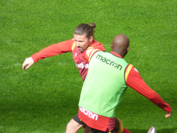 Zwei Männer in Fußballschuhen auf einem hellen, sonnigen grünen Feld.