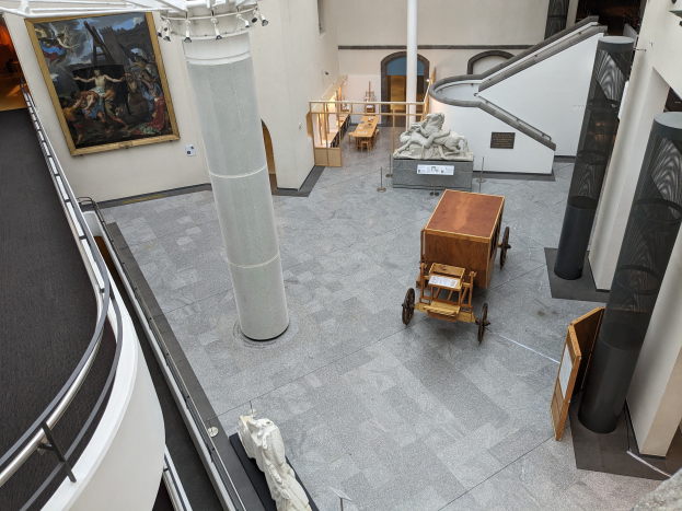 Eine große Galerie mit zahlreichen Statuen, Vitrinen, Tischen, Säulen, Infotafeln, gerahmten Kunstwerken und Leuchten, wahrscheinlich das Nationalmuseum für Kunst.