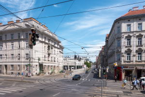 Eine Stadtstraße mit Autos, Fußgängern, Gebäuden, Strommasten, Verkehrszeichen, Schildern, Bäumen und einem bewölkten Himmel.