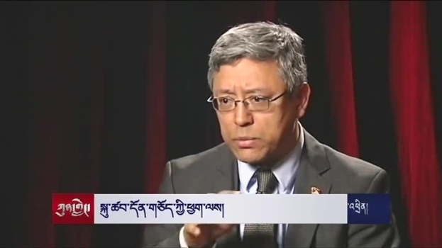 Ein Mann im Anzug mit Brille spricht vor einem dunklen Hintergrund in ein Mikrofon, mit einem Wasserzeichen, das eine Aussage über das Wirtschaftswachstum von Bangladesch enthält.