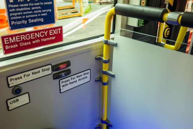 Notausgangsschild an einer Zugseite mit einer Tür, einem Griff und einem Glasfenster, das eine Straße, Pfosten und Außenobjekte zeigt.