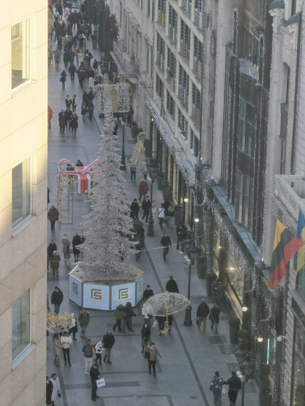 Eine belebte Stadtstraße mit Menschen zwischen hohen Gebäuden, mit einem großen geschmückten Weihnachtsbaum in der Mitte.