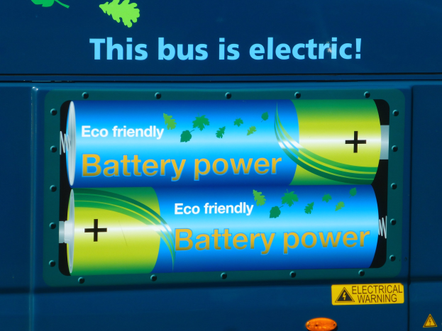 Blauer elektrischer Bus mit "Dieser Bus ist elektrisch"-Schild und zwei seitlich angebrachten Batterien.