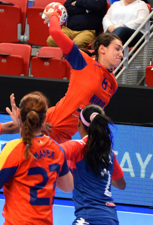 Eine Gruppe von Frauen, die Handball in einem Stadion spielt, mit einer, die den Ball hält und Zuschauern im Hintergrund.