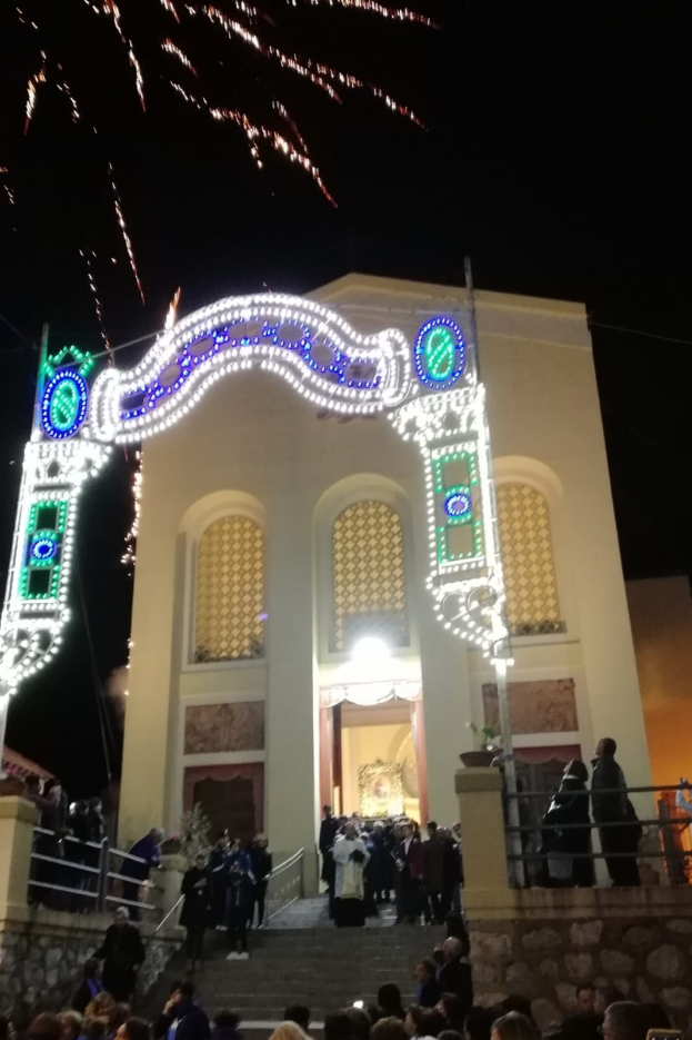 Menschen vor einem Gebäude mit einem bogenförmigen, beleuchteten Eingang, Treppen mit Geländern und Topfpflanzen, die Silvester mit Feuerwerk feiern.